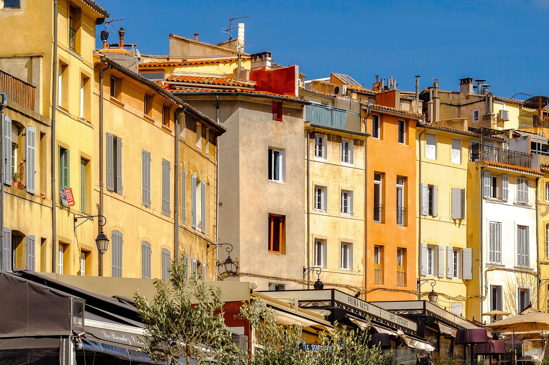 Sunlit ochre and yellow façades with painted shutters above café terraces in the historic centre of Aix-en-Provence