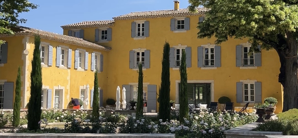 Ochre-yellow Provençal bastide with blue shutters, cypress trees and rose garden