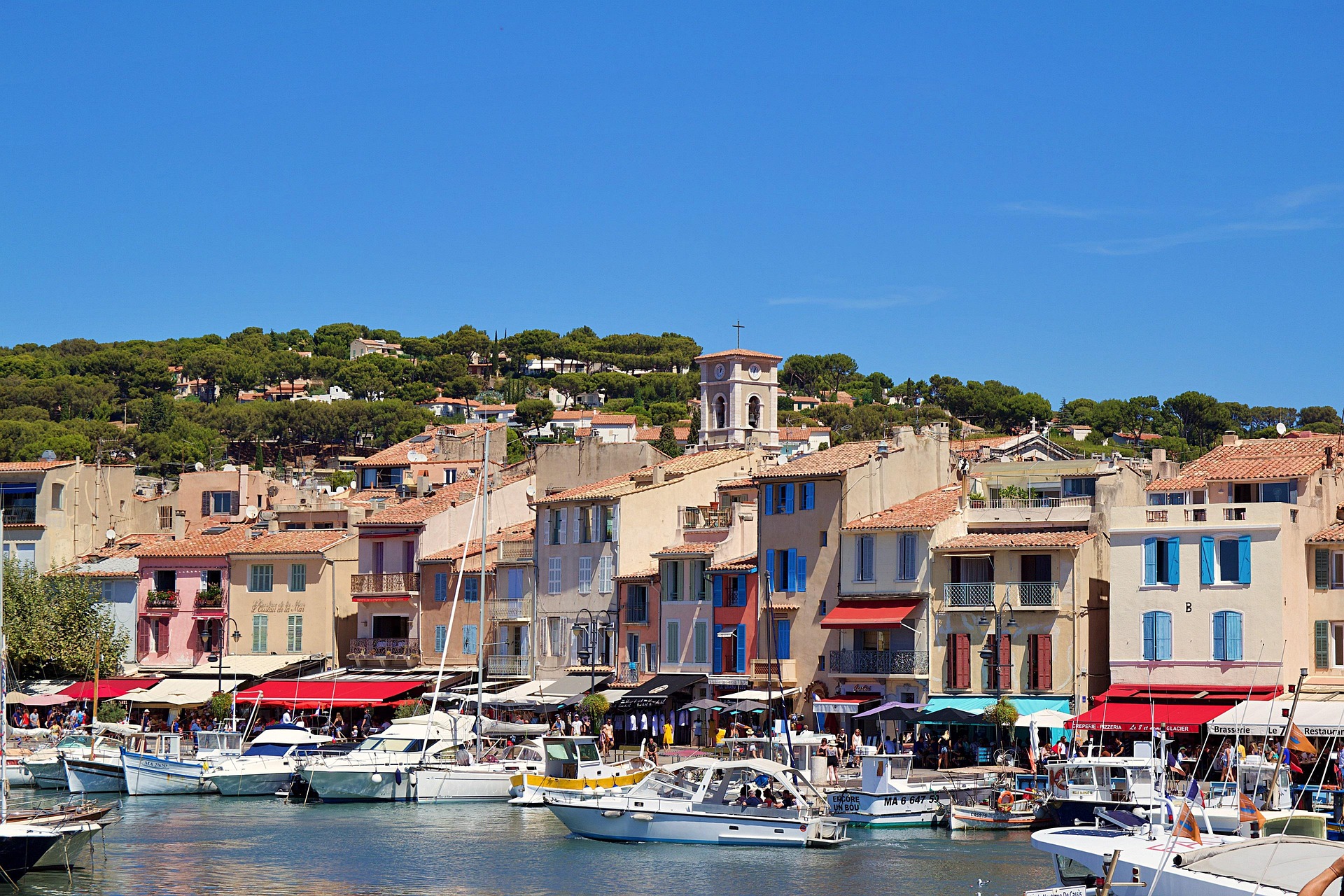 The colourful harbour of Cassis with fishing boats moored in front of pastel façades and the bell tower on the hill behind